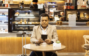Gicelmo olhando o tablet numa cafeteria de aeroporto, enquanto aguarda o próximo vôo internacional